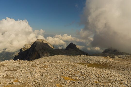 View of rocky terrain meeting distant mountain peaks under a sky brushed with soft clouds, a serene vista captured in Triglavski narodni park, Gorenjska, Slovenia.