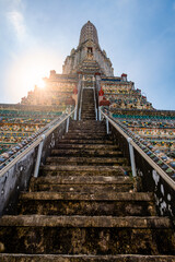 Detailed view of the ornate towers of Wat Arun in Bangkok, Thailand, showcasing rich ceramic floral patterns, sculpted figures, and intricate decorations under bright daylight.