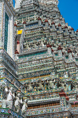Detailed view of the ornate towers of Wat Arun in Bangkok, Thailand, showcasing rich ceramic floral patterns, sculpted figures, and intricate decorations under bright daylight.