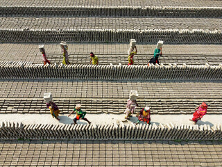 Narayanganj, Bangladesh - 11 February 2024: Aerial view of workers carrying loads of bricks, their colorful clothing contrasting against the monochrome landscape of the brickyard.