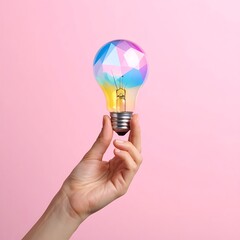 Hand holds a lightbulb with facets painted in rainbow colors, set against a soft pink background