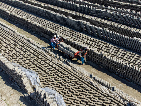 Narayanganj, Bangladesh - 09 November 2024: Aerial view of rows of bricks drying, with workers transporting them on a small vehicle, creating a textured landscape under the sun..