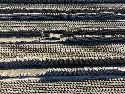 Narayanganj, Bangladesh - 09 November 2024: Aerial view of rows of bricks under the sun, with a lone worker pushing a cart through the textured landscape.