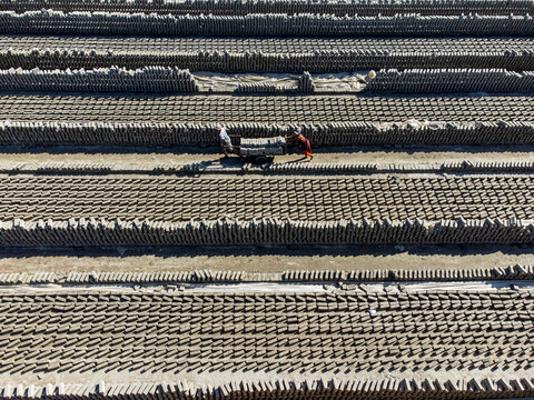 Narayanganj, Bangladesh - 09 November 2024: Aerial view of workers pushing carts through endless rows of sun-baked bricks, creating a textured landscape under the open sky.