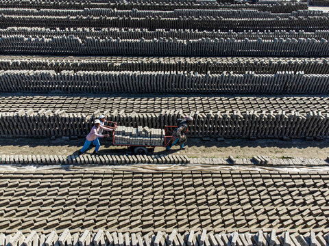 Narayanganj, Bangladesh - 09 November 2024: Aerial view of workers pushing carts through a brickyard, the landscape a symphony of earthy tones and regimented patterns.