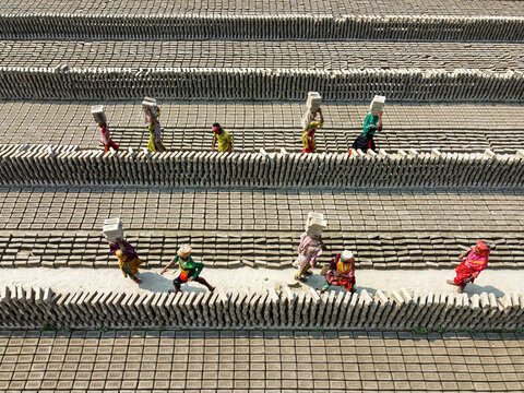Narayanganj, Bangladesh - 11 February 2024: Aerial view of workers carrying loads of bricks, their colorful clothing contrasting against the monochrome landscape of the brickyard.