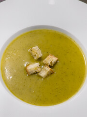 Creamy vegetable soup is served hot in a white bowl, topped with crunchy bread croutons, offering a simple homemade starter for a comforting family meal in a cozy home kitchen.