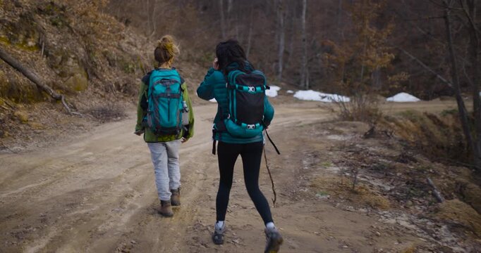 Two Female Friends Hiking on a Mountain Dirt Road, Enjoying Nature and Leftover Snow Patches