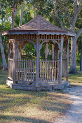 Wooden Gazebo and Park Bench in a Lush Urban Park Setting. Rustic wooden gazebo and a vibrant orange park bench under a lamppost in a green park. The peaceful ambiance and bright vegetation symbolize 