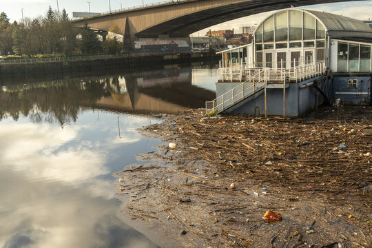 Glasgow, United Kingdom - 22 November 2025: View of the River Clyde's murky waters reflecting the sky, contrasted by the debris-strewn banks near the iconic Glasgow Arc bridge.