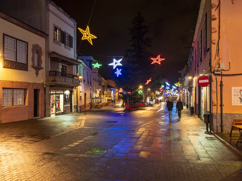 San Cristobal de La Laguna, Spain - 17 December 2016: View of a quiet street adorned with twinkling Christmas stars, as two figures stroll under the warm glow of streetlights.