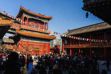 Beijing, China - 26 November 2025: View of the Yonghe Temple's vibrant architecture contrasting against the clear sky as crowds gather below, their presence a bustling symphony of movement.