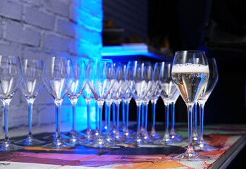 Elegant champagne glasses arranged in a row on a colorful table, reflecting soft blue lighting, creating a festive atmosphere for celebration and enjoyment