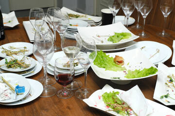 Leftover food and dirty dishes scattered across a wooden table, featuring empty wine glasses and plates, creating a post-event atmosphere of culinary indulgence and celebration