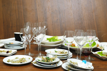 Leftover food and dirty dishes scattered on a wooden table after an event, featuring empty glasses and plates, showcasing the aftermath of a lively gathering with remnants of a meal