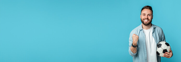 A man with a beard is smiling widely while holding a soccer ball under his arm. He has a fist...