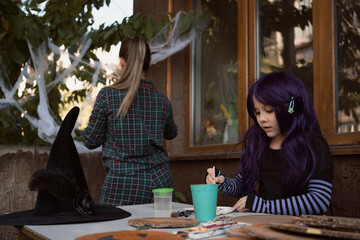 Little girl wearing purple wig and witch costume painting by paint and brush while mom decorate house