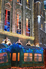 Obraz premium Colorful festive train decorated with bright lights is parked in front of a beautifully illuminated building, creating a magical winter wonderland atmosphere for holiday celebrations