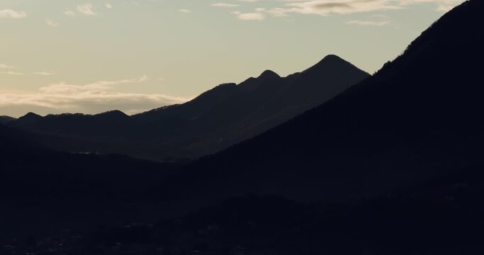 Aerial view of the dark, imposing mountain silhouettes against a soft, pale sky, creating a stark contrast of light and shadow, San Michele di Serino, Irpinia, Italy.