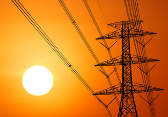 Electricity pylons and power lines silhouetted against a bright sun in a warm light setting