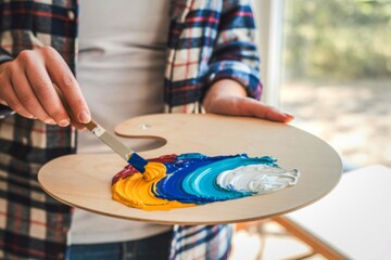 Artist mixing colorful paints on a wooden palette with a palette knife