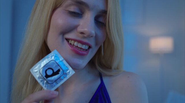 Seductive woman holding a condom with a playful expression, promoting safe sex and intimacy awareness