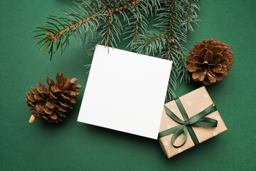 Square Merry Christmas greeting card mockup with blank space for design or congratulations messages, surrounded by evergreen branches, pine cones, and a beautifully wrapped gift box