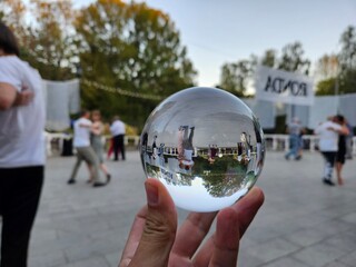 Person holding a glass ball with a reflection of people dancing in the background with text Ronda