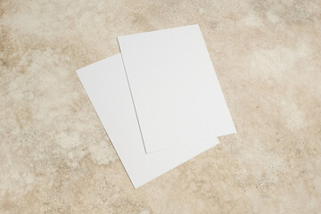 Fototapeta premium Two blank white sheets of paper stacked on a textured beige surface, ideal for design mockups, presentations, or creative projects with ample copy space for text