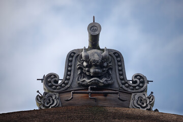 An ancient Japanese temple roof is adorned with an Onigawara carved with striking detail