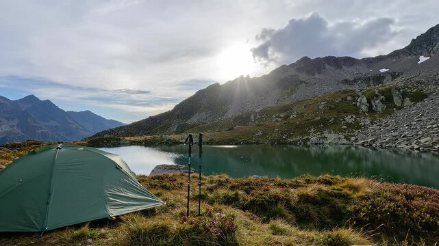 Green Tent Set Near Lake with Mountains Landscape and Trekking Poles in Bright Sunlight
