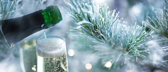 Bottle of champagne and filled glasses outdoors in front of frozen pine branches with bright bokeh lights. Background for christmas and new year's celebrations. Close-up. 