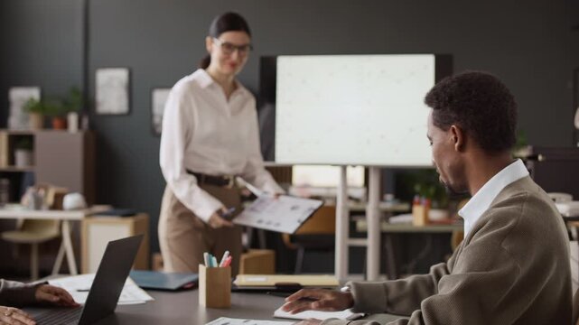 Brunette woman with clipboard in hand asking African American colleague to continue presentation during conference