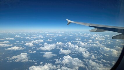 View of the sky and clouds from an airplane window with in-flight wing visible.