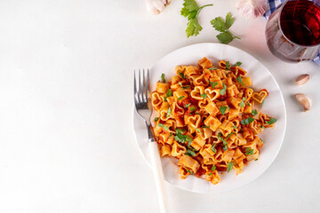 Heart shaped pasta with tomato sauce. Classic italian marinara or bolognese pasta with fresh herbs, simple and delicious recipe for Valentine day or date night, on white table copy space