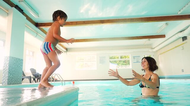 Indoor swimming pool in salmon arm, canada, showing a mother encouraging her son to jump from the poolside, culminating in a joyful embrace in the water