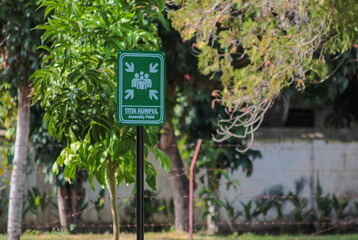 Green emergency assembly point sign outdoors among trees