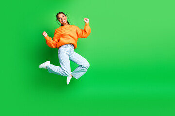 Young woman in orange knitwear jumps joyfully against a green background conveying energy and fashion lifestyle advertising and youthful branding