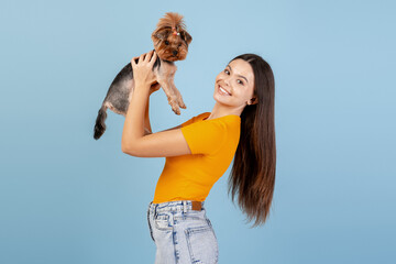 Smiling young woman holding up her Yorkshire Terrier dog, showing pet love and companionship