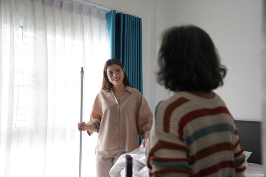 Caregiver helping elderly woman making bed at home