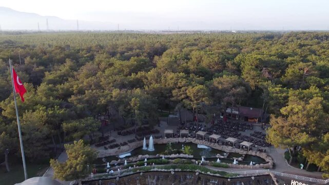 Aerial drone flyaway from Atat&uuml;rk head monument in Antalya at sunset. Waterfall flowing from cliff surrounded by green park and forest. Ungraded, DLog
