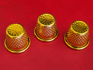 Three gold colored thimble on red for sew