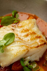 A beautifully grilled fish fillet rests atop a colorful mix of sautéed vegetables, garnished with fresh herbs. The natural colors and textures create a delightful culinary experience