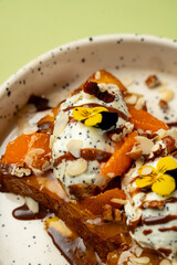 A tempting dessert showcases soft bread topped with rich ice cream, succulent orange slices, crunchy nuts, and vibrant edible flowers. Perfect for a sweet treat