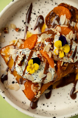 A charming dessert displays juicy peaches adorned with creamy toppings, sprinkles of nuts, and vibrant edible flowers. Perfect for savoring on a sunny day