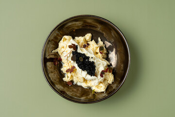 A bowl presents luscious creamy pasta adorned with glossy caviar and vibrant microgreens. The dish captures a moment of culinary elegance in a cozy setting