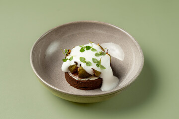 A delicious dessert sits in an elegant bowl, featuring a soft sponge topped with creamy yogurt, fresh herbs, and hints of fruit. This artistic creation invites a delightful tasting experience