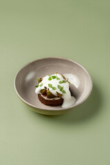 A beautifully crafted dessert is displayed on a simple, earthy plate. The rich chocolate base is topped with creamy yogurt and adorned with fresh herbs, inviting a taste of elegance