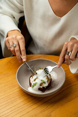 A person carefully cuts into an intricately plated dish featuring layers of flavors. The foamy topping adds an artistic flair, making the meal visually stunning and appetizing