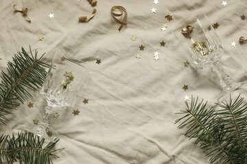 Golden star confetti tinsel, beige linen table cloth background. Champagne glasses. Fir branches floral frame, copy space. Christmas party concept. New Years flatlay, top view. Festive holiday banner